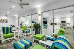 A modern living room with white furniture, green cushions, and a large window overlooking a kitchen. - Bright mid-century modern home w/ private pool and spa, gas grill, dogs welcome (Palm Springs)