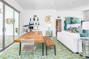 A modern living room with a wooden dining table, white sofa, and decorative wall art. - Bright mid-century modern home w/ private pool and spa, gas grill, dogs welcome (Palm Springs)