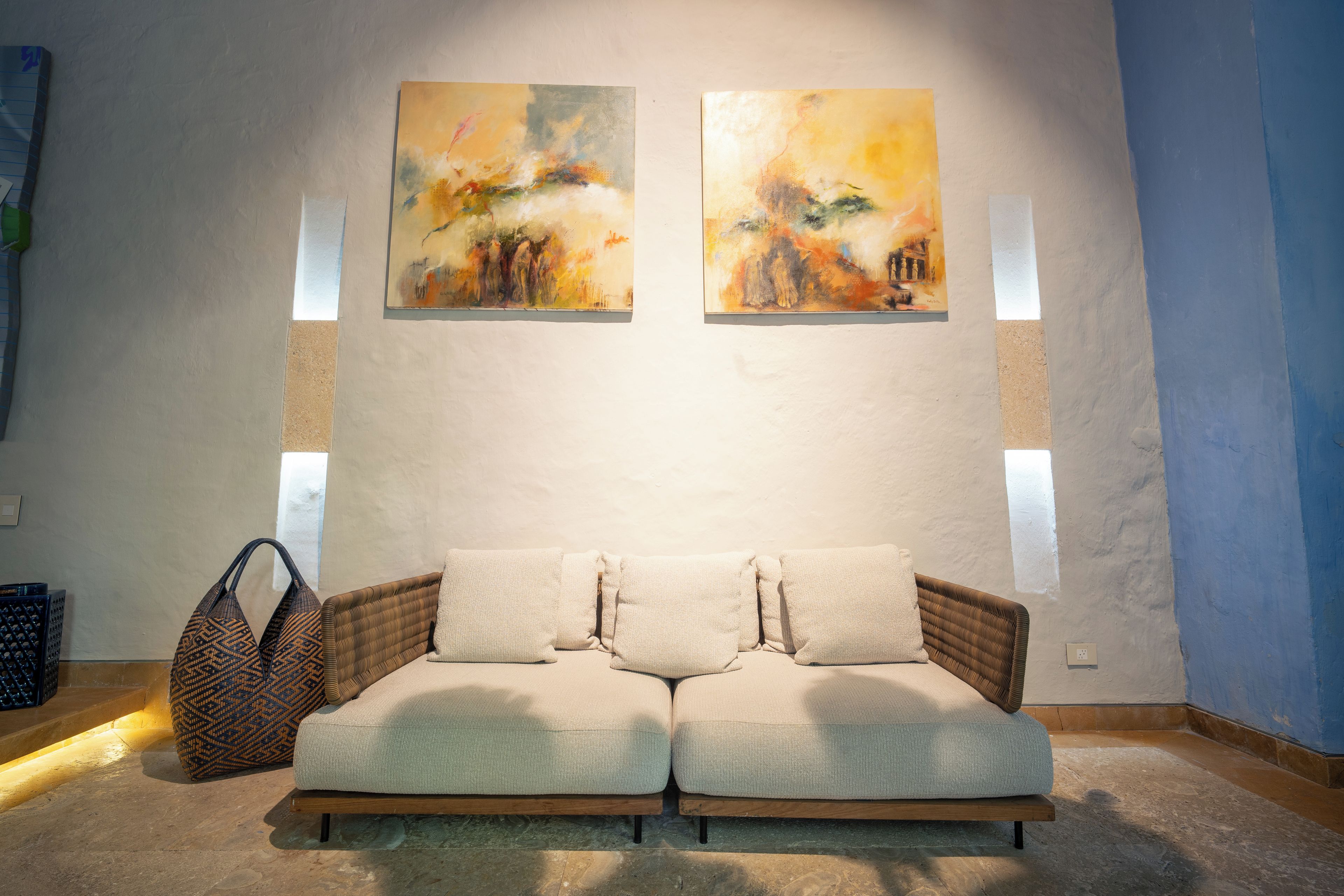 A room with a sofa, two paintings on the wall, and a window.