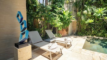 A poolside area with lounge chairs and a laptop on a stand, surrounded by lush greenery and a clear pool.