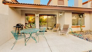 Un patio con una mesa, sillas, una parrilla y un cactus.