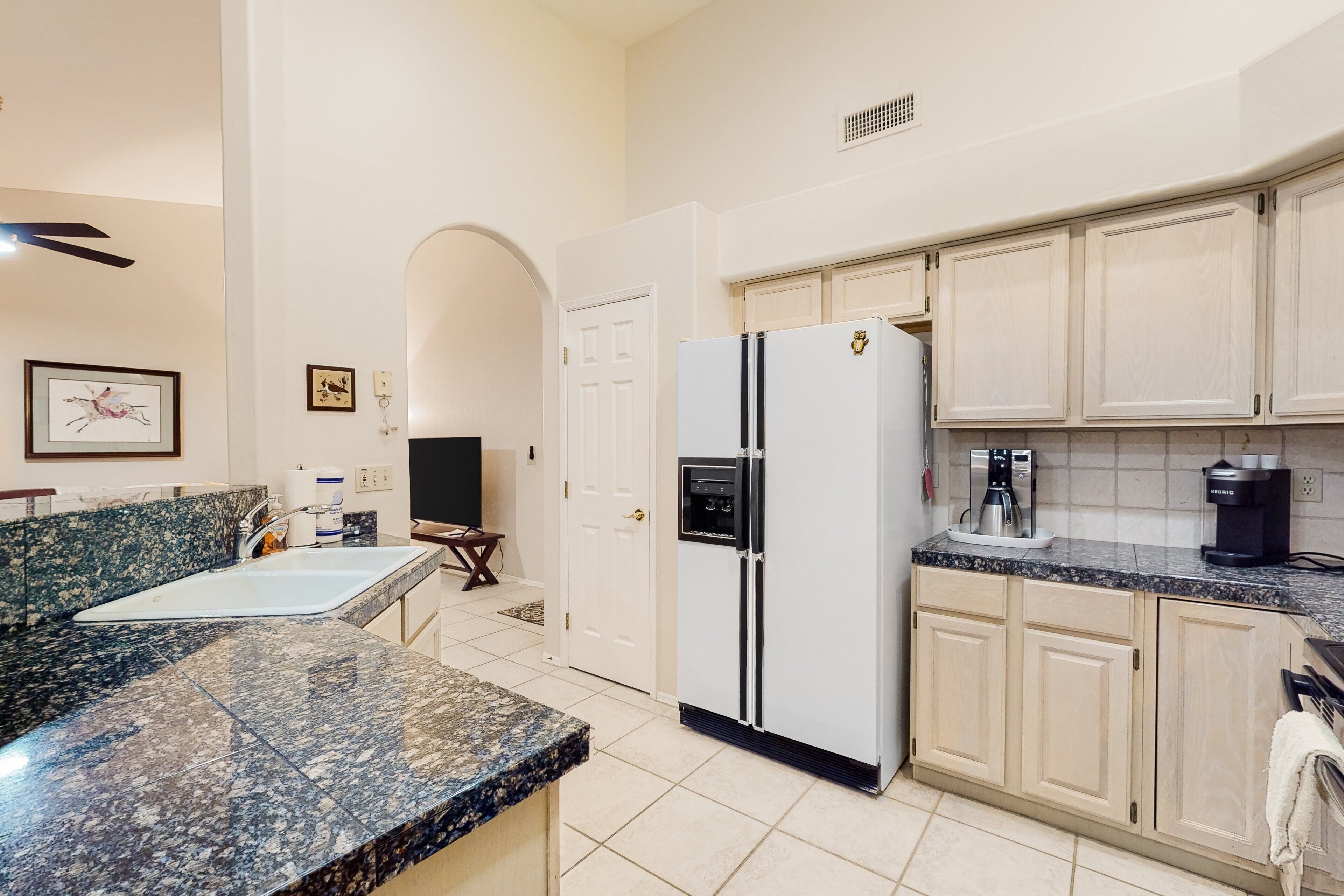 A kitchen with a granite countertop, a refrigerator, cabinets, a sink, and a coffee maker.