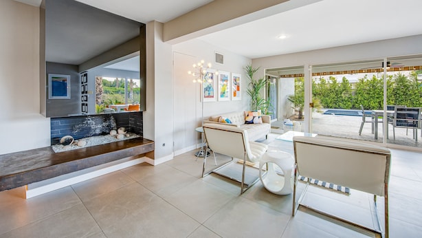 A modern living room with a fireplace, a dining area with a white table and chairs, and a large glass door leading to an outdoor patio. - Mid-century modern home with private pool, spa, grill & mountain views (Palm Springs)
