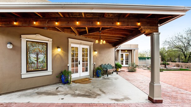 Un patio abrité avec un plafond en bois, une porte à panneaux de verre et une plante en pot près de l’entrée.