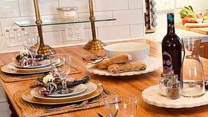 Une cuisine bien rangée, avec une étagère en verre, une bouteille de vin, des salières et des poivrières, et une planche à découper avec des légumes.