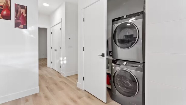 Un cuarto de lavado con dos lavadoras de carga frontal, una pared de azulejos blancos y piso de madera.