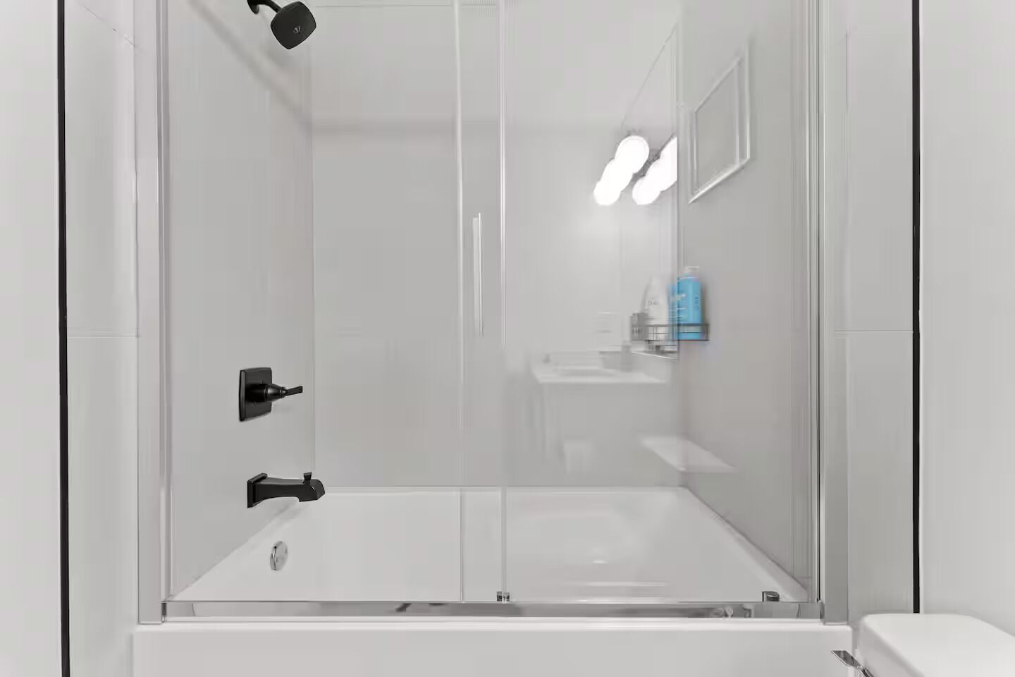 A modern shower enclosure with a glass door, a black faucet, and a white sink with a mirror above it.