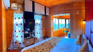 A cozy wooden cabin bedroom with a bed, a built-in wardrobe, a window with a view, and a small seating area. - Poets inn (Pahalgam)
