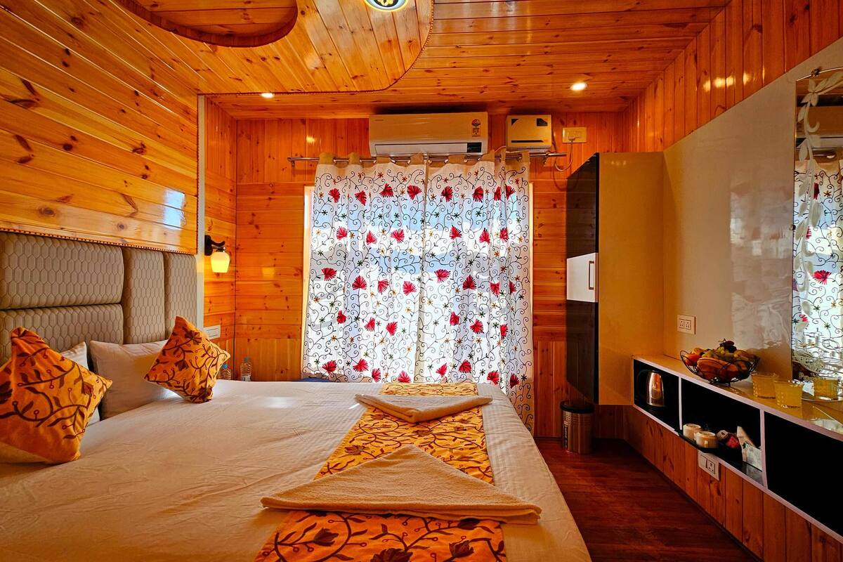 A wooden cabin bedroom with a bed, pillows, a bedside table, and a mirror.