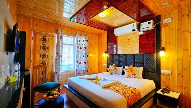 A wooden room with a bed, a TV, and a window with curtains. - Poets inn (Pahalgam)