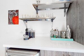 Eine Küchenarbeitsfläche mit weißer Arbeitsplatte, einem Edelstahlregal und verschiedenen Küchenutensilien, darunter eine Kaffeemaschine, ein Mixer und Gläser.