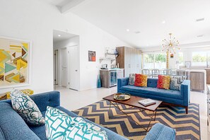 Ein modernes Wohnzimmer mit einem blauen Sofa, einem gemusterten Teppich und einem Essbereich mit einer Chandelieber.
