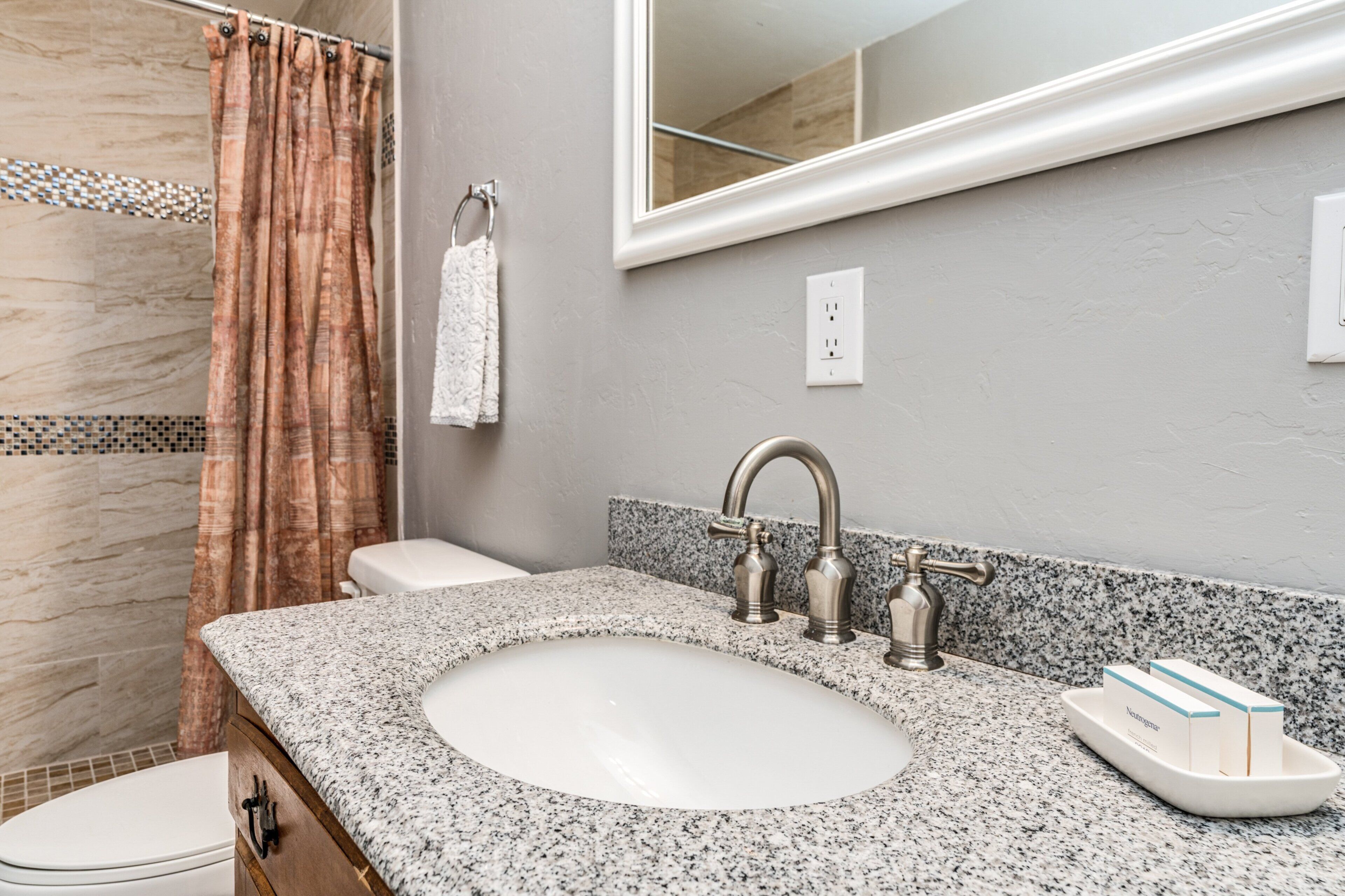 A bathroom with a granite countertop, a sink, a mirror, a shower curtain, and a towel rack.