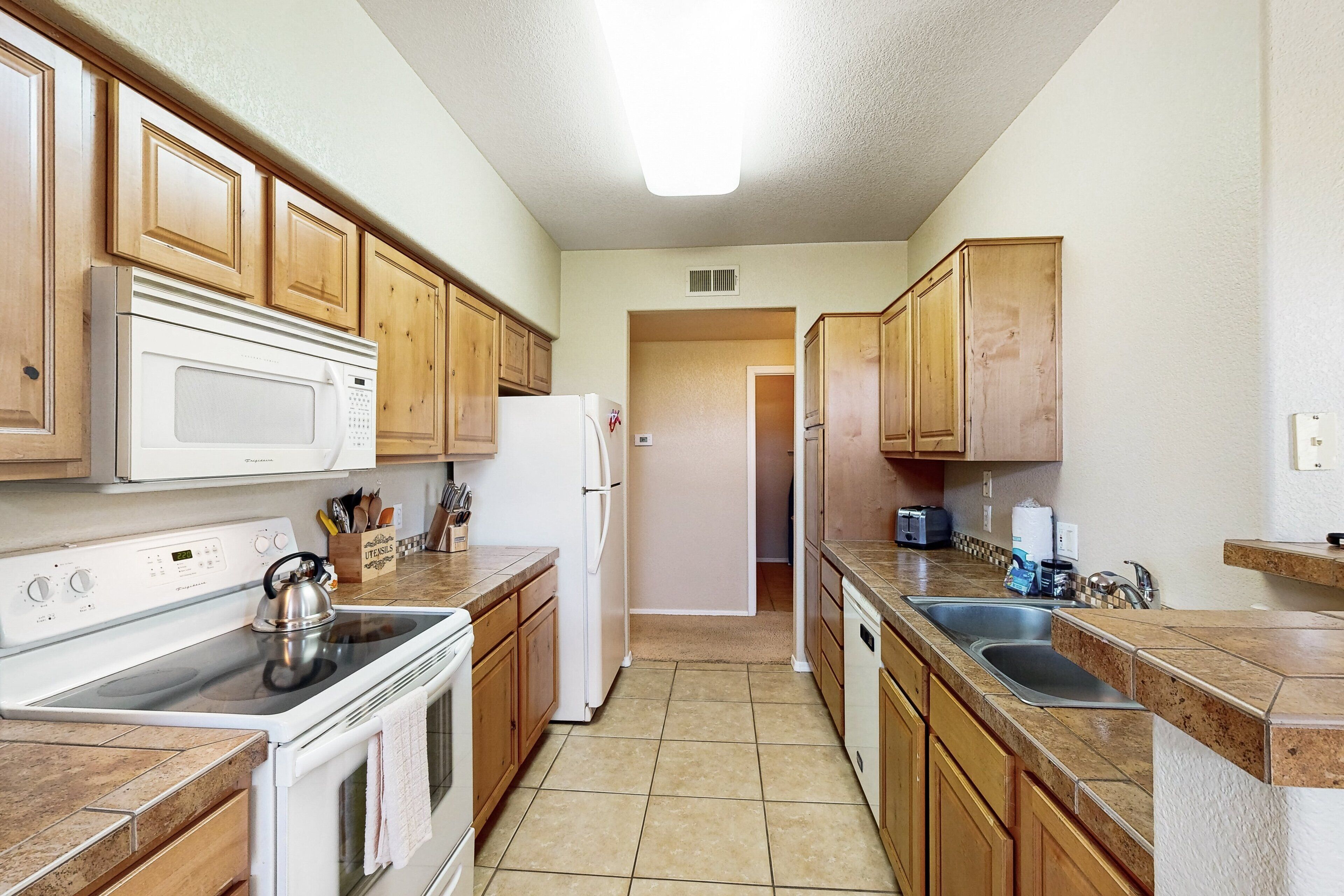 A kitchen with wooden cabinets, a stove, a microwave, a refrigerator, and a sink.