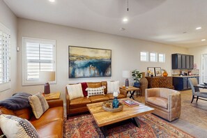 A spacious living room with a brown leather sofa, a wooden coffee table, and a large abstract painting on the wall. - Dog-friendly golf course-adjacent home with a private pool, pool spa, & AC (Indio)