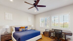 Ein Schlafzimmer mit Bett, Schreibtisch, Stuhl und Deckenventilator.