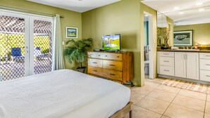 Une chambre à coucher comprenant un lit, une télévision, une commode en bois et une porte-fenêtre coulissante donnant sur un balcon.