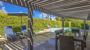 Un espace extérieur aménagé avec une terrasse, une pergola, des chaises longues, une table à manger et une piscine.