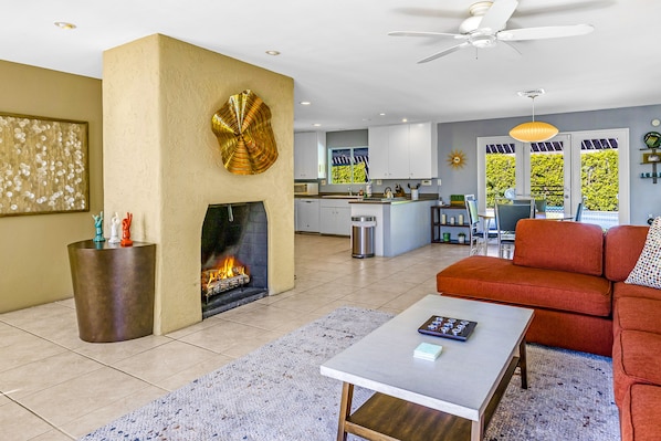 A modern living room with a fireplace, a dining area, and a kitchen in the background. - Marvelous, Dog/Family-Friendly House w/Private Grill, Outdoor Pool, Attached Spa (Palm Springs)