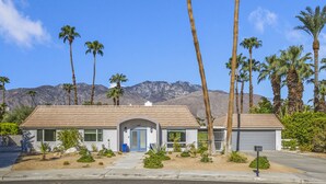 Une maison de plain-pied avec un garage, entourée de palmiers et avec des montagnes en arrière-plan.
