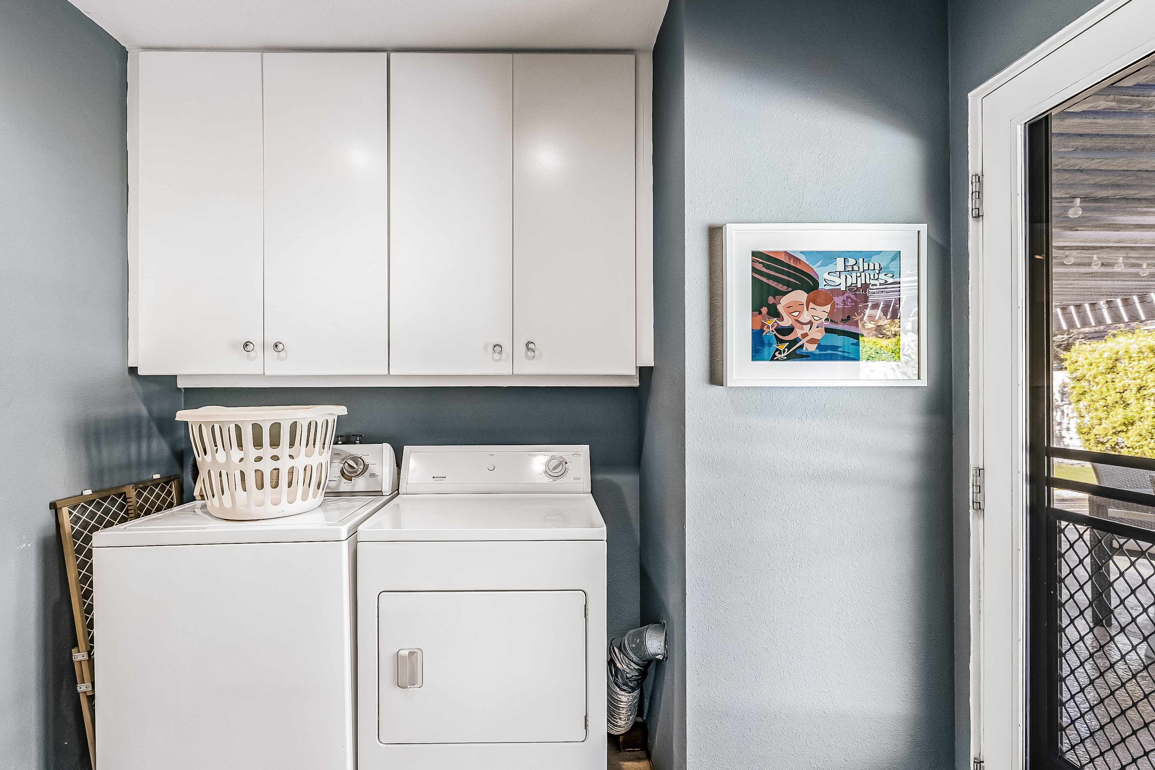 A laundry area with a white washer and dryer, a laundry basket, and a framed picture on the wall.