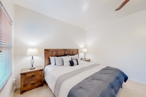 Un dormitorio con una cama grande, cabecera de madera, mesitas de noche con lámparas y una ventana con persianas.