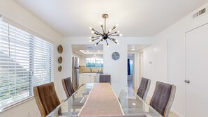 A dining area with a glass table, chairs, and a modern chandelier. - Gated resort condo with outdoor pool, hot tub, & tennis - walk to dining (Palm Springs)