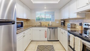 A modern kitchen with stainless steel appliances, white cabinets, a window with blinds, and a patterned rug. - Gated resort condo with outdoor pool, hot tub, & tennis - walk to dining (Palm Springs)