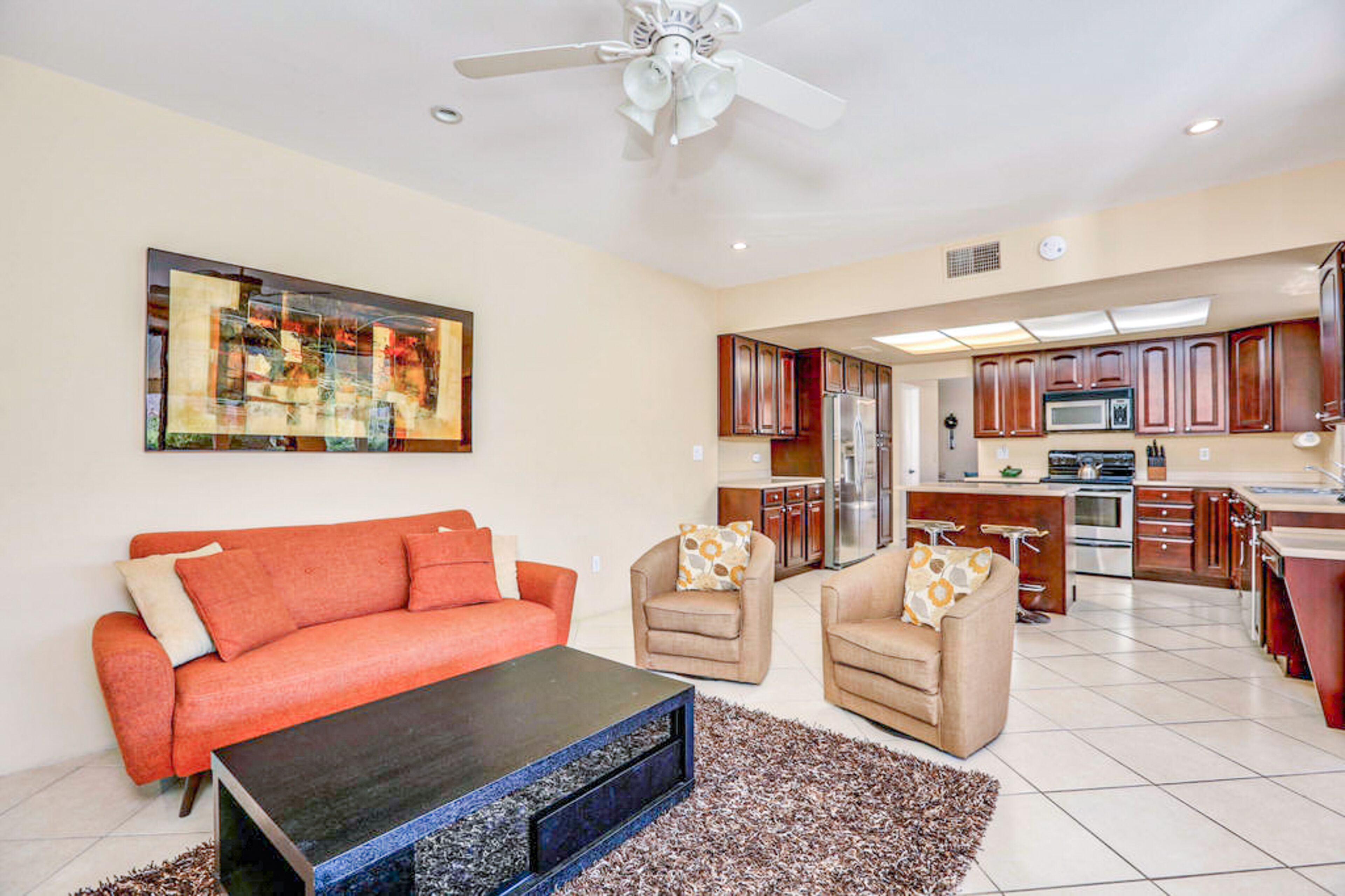 A living room with a sofa, two armchairs, a coffee table, and a ceiling fan.