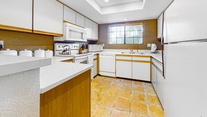 Una cocina moderna con armarios blancos, un microondas, una tetera y un ventanal.