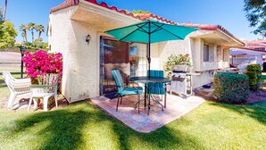Un patio con mesa y sillas, una parrilla y un área cubierta.