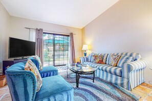 A living room with a sofa, ottoman, and a flat-screen TV. - Inviting, dog-friendly condo with outdoor pool, pool spa & tennis access (Palm Springs)