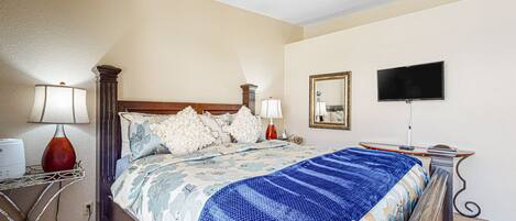 A hotel room with a bed, bedside lamps, a flat-screen TV, and a mirror on the wall.