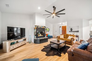 Ein modernes Wohnzimmer mit Flachbildfernseher, Holz-Unterhaltungseinheit, schwarzem Kamin und Deckenventilator.