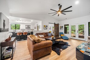 A spacious living area with a leather sofa, a coffee table, and a dining table. There is a kitchen in the background with bar stools. - Ground-floor mountain-view home with patio, central AC & washer/dryer (Sedona)