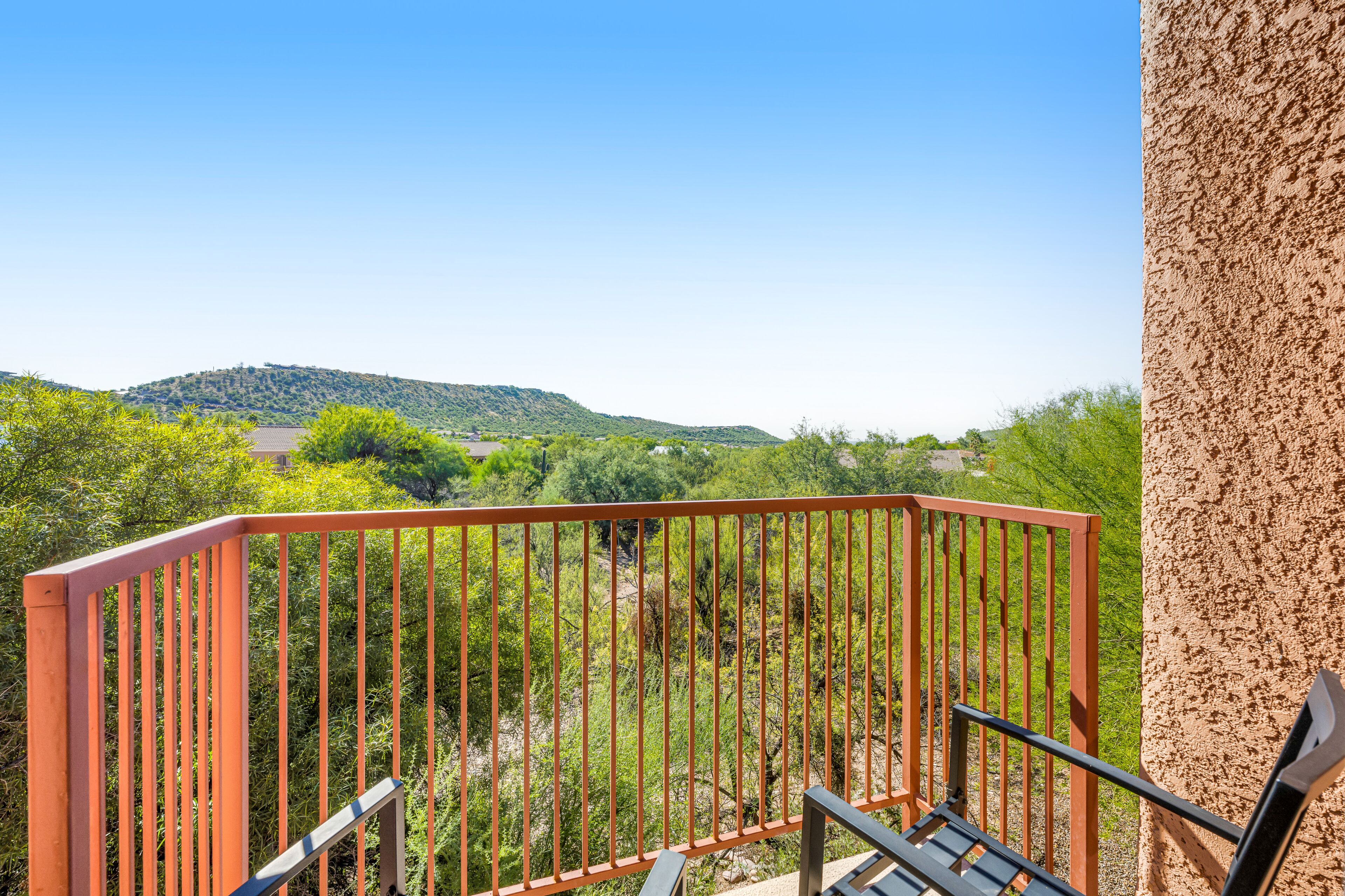 A balcony with a metal railing overlooking a green landscape with hills.