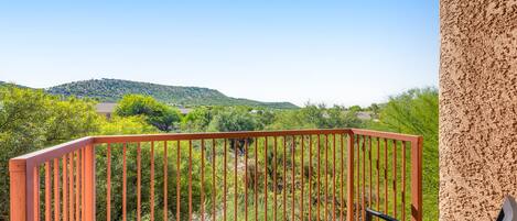 A balcony with a metal railing overlooking a green landscape with hills.