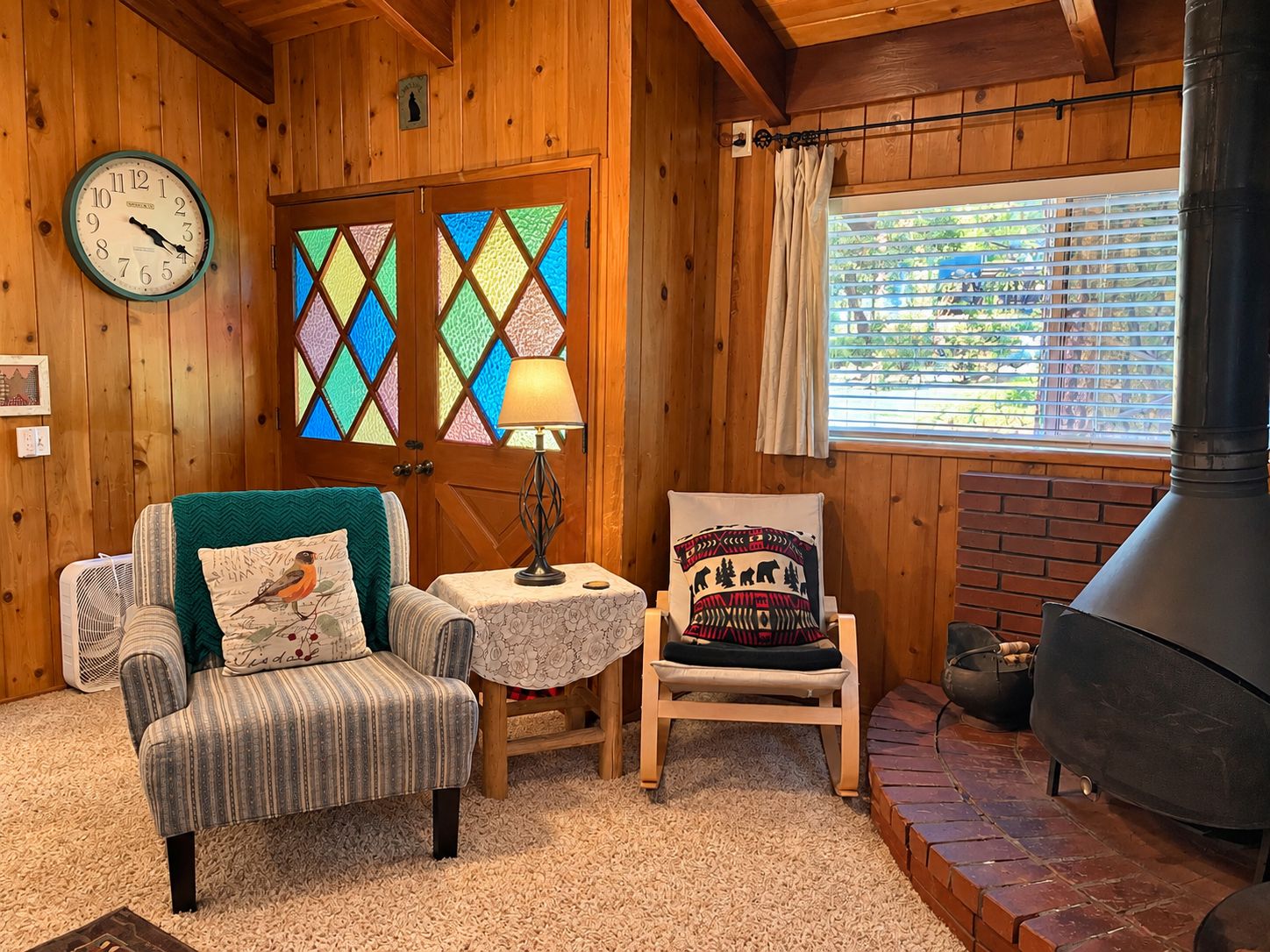 A cozy room with a wooden interior, a clock, a fireplace, and a window with blinds.