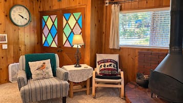 A cozy room with a wooden interior, a clock, a fireplace, and a window with blinds.