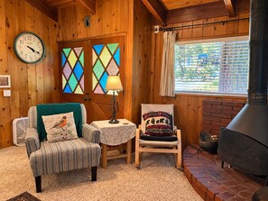 Una habitación acogedora con paredes de madera, un reloj, una chimenea y una ventana con persianas.