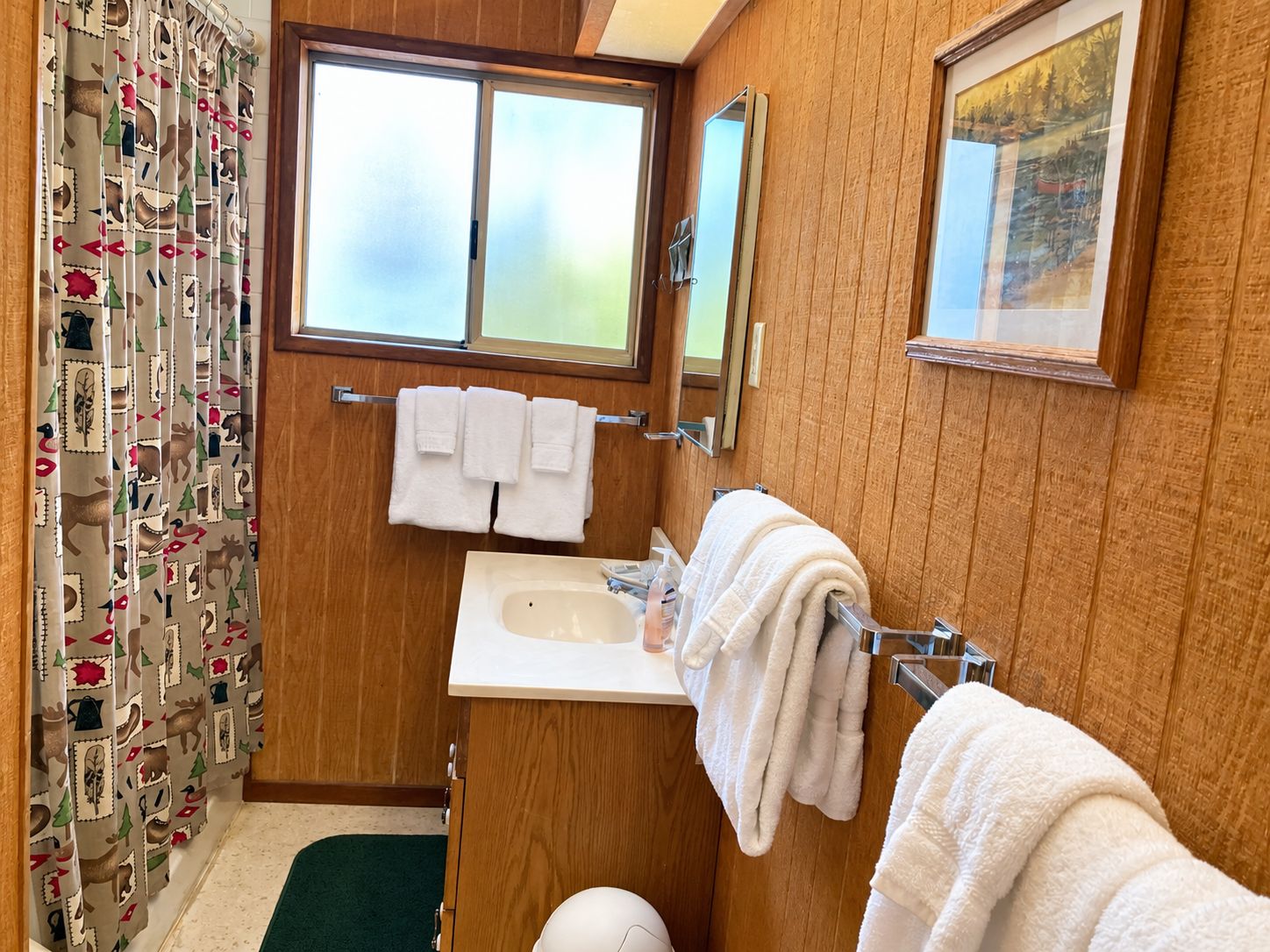Een badkamer met een houten wastafelmeubel, een wastafel, een spiegel en een raam.