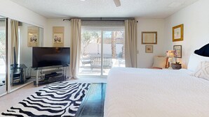 A bedroom with a bed, a TV on a stand, a ceiling fan, and a view of the outside. - Recently Updated Home w/ Private Patios: 15 Mins From Downtown Palm Springs (Desert Hot Springs)