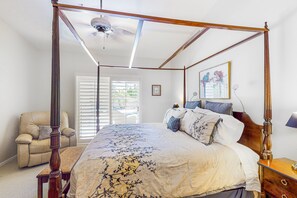 A four-poster bed with a canopy, a wooden nightstand, a bedside table, a chair, and a window with blinds. - Dog-friendly home with private pool & spa, outdoor kitchen area (Cathedral City)