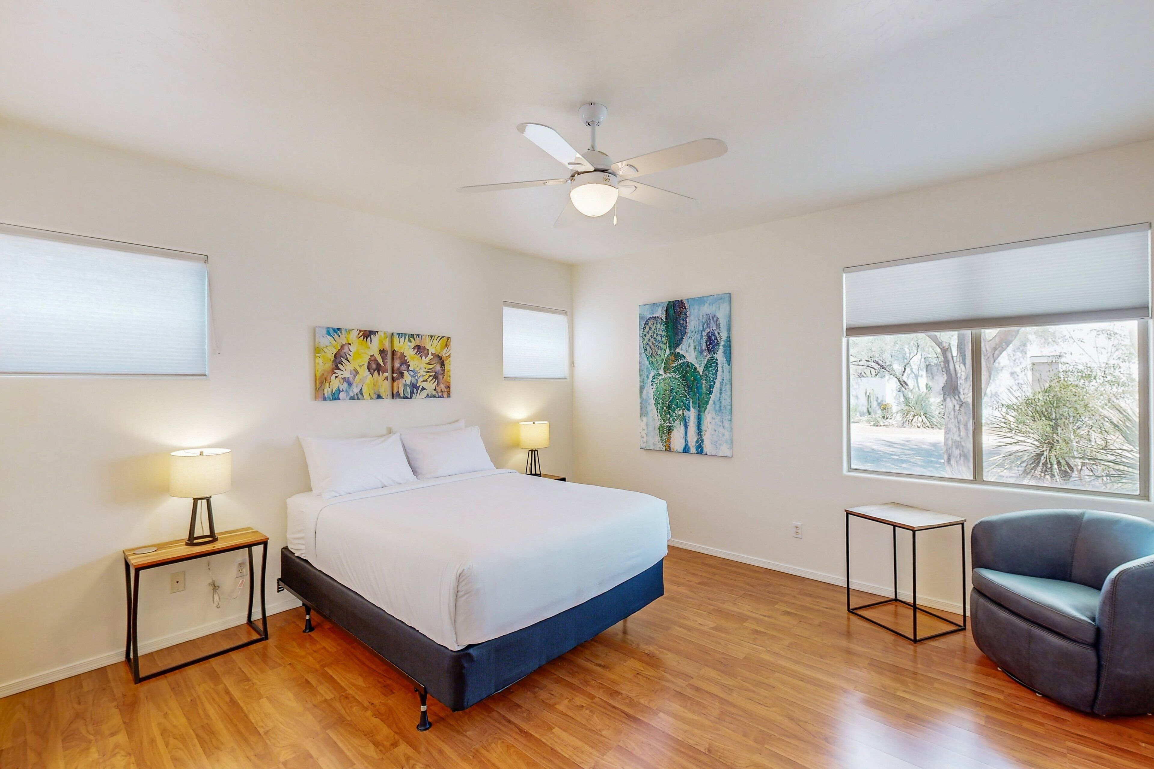 Une chambre à coucher avec un lit, un ventilateur de plafond, deux tableaux, une fenêtre et une chaise.