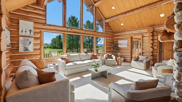 A log cabin interior with a large living area, multiple seating arrangements, and large windows offering a view of the outdoors. - Heber Gathering Lodge, Game Room, Sleeps 32 (Heber City)