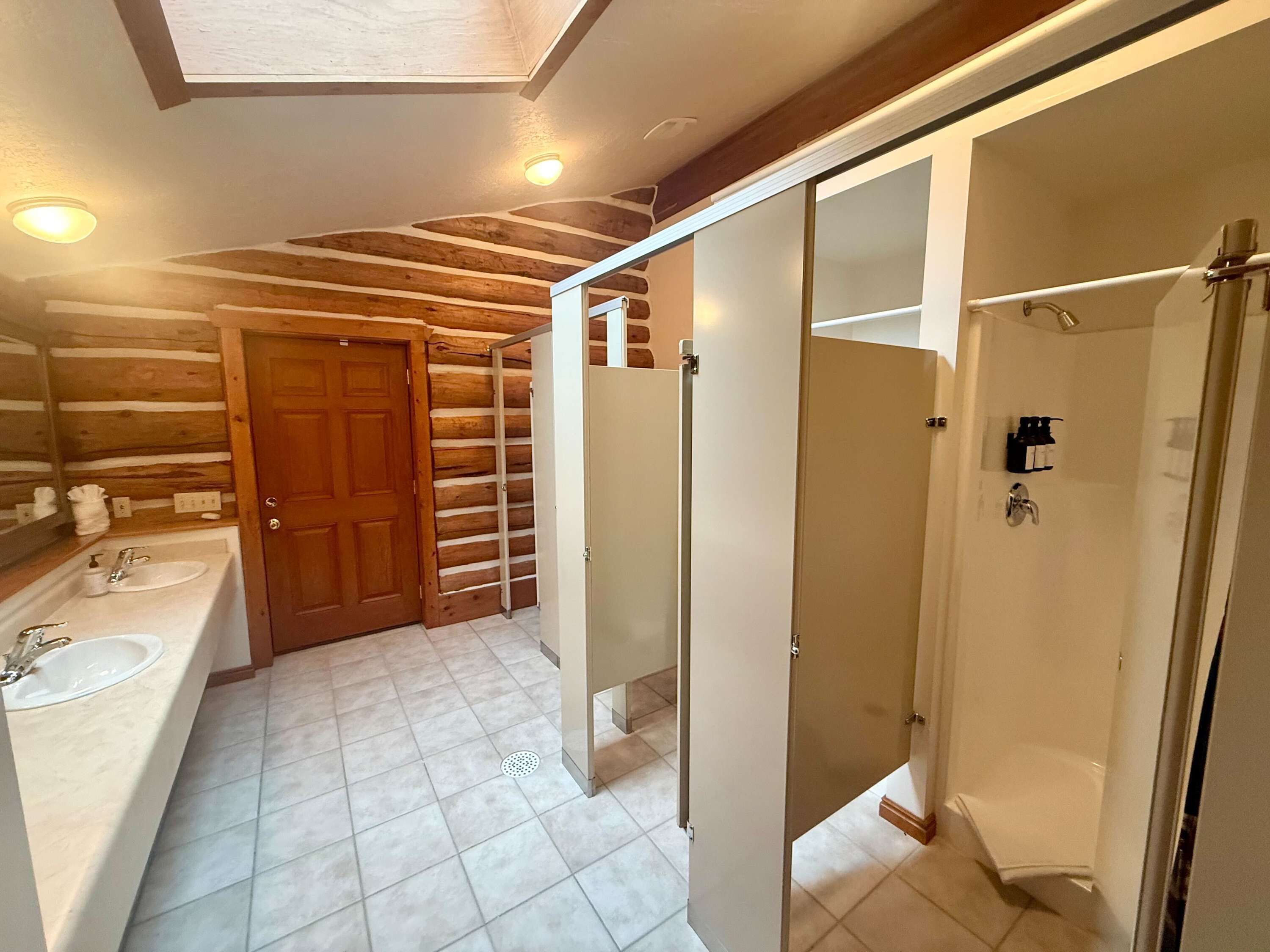 Une salle de bain avec un plafond en bois, un grand miroir, deux lavabos, une douche et des toilettes.