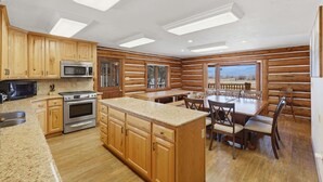A kitchen with wooden cabinets, a granite countertop, stainless steel appliances, and a dining area with a table and chairs. - Heber Gathering Lodge, Game Room, Sleeps 32 (Heber City)
