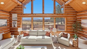 A log cabin interior with a large window, a sofa, a chair, and a small table. - Heber Gathering Lodge, Game Room, Sleeps 32 (Heber City)