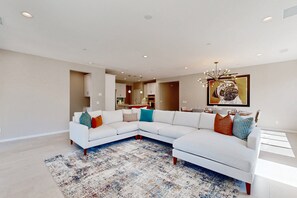 A modern living room with a sectional sofa, a patterned rug, and a large painting on the wall. - Modern home with gas fireplace, mountain views, large yard (Cathedral City)