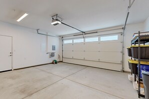 Eine geräumige Garage mit großer Tür, einer Deckenleuchte und einem Metallregal mit Aufbewahrungsbehältern.